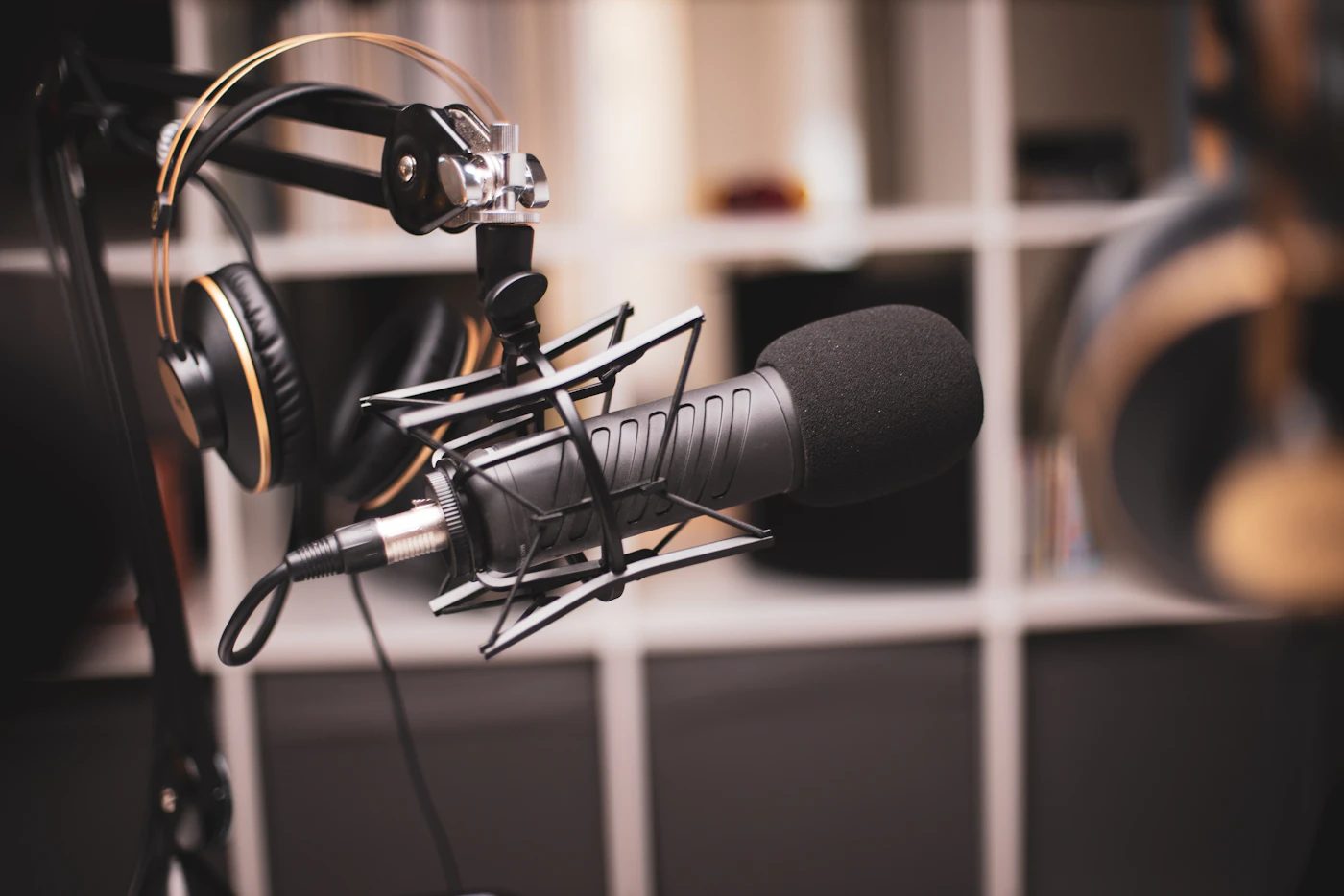 Studio microphone in a shock mount with headphones hanging behind it
